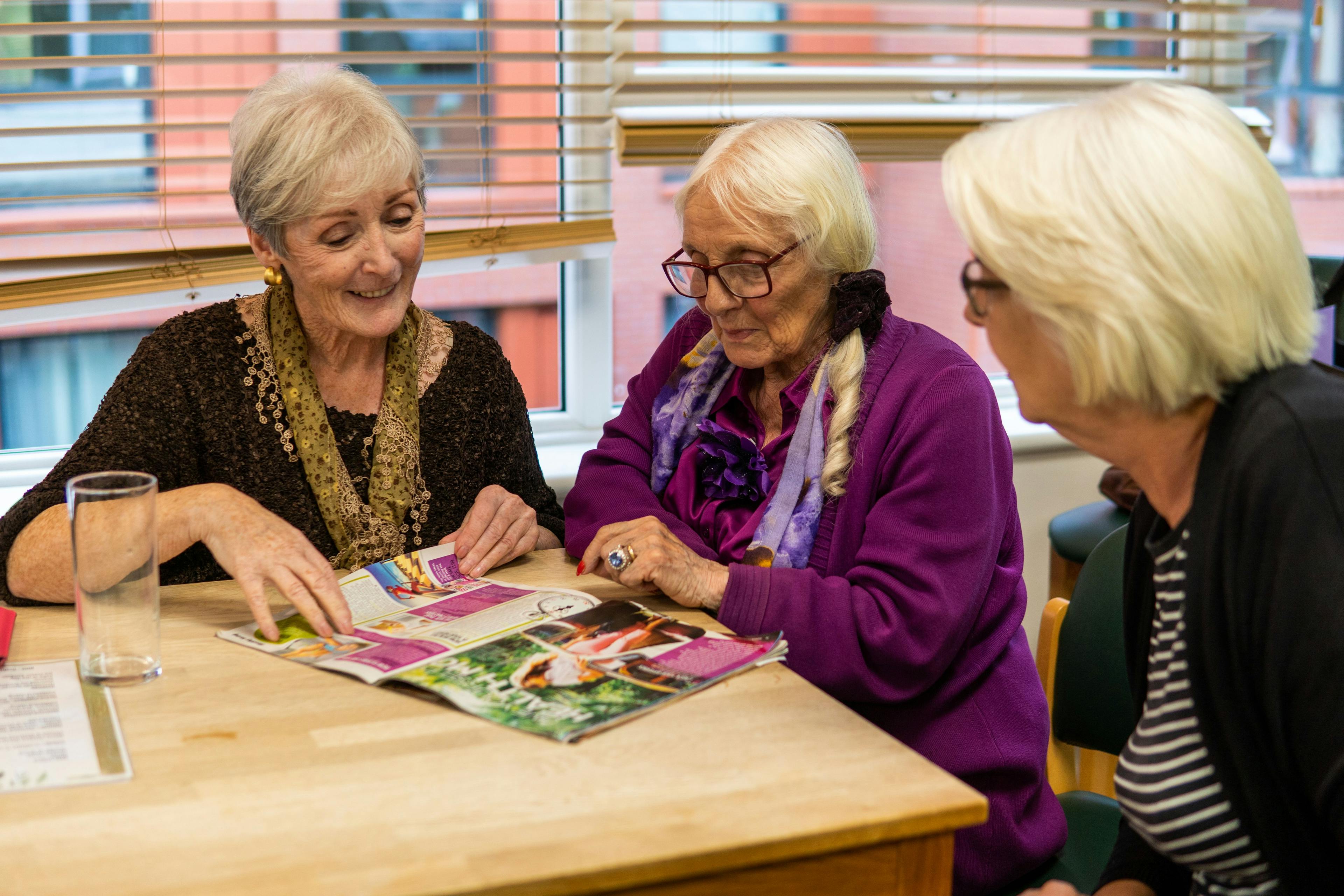 Middle aged female carer sat with two women looking at a magazine